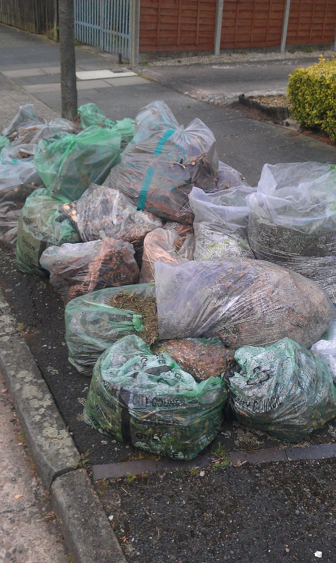 Pile of bagged green garden waste stacked at the kerbside for collection
